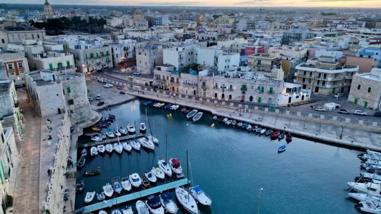 Malowniczy widok lotniczy na marinę Giovinazzo o zachodzie słońca w Apulii we Włoszech. Uwydatnia zacumowane łodzie i zabytkową architekturę.