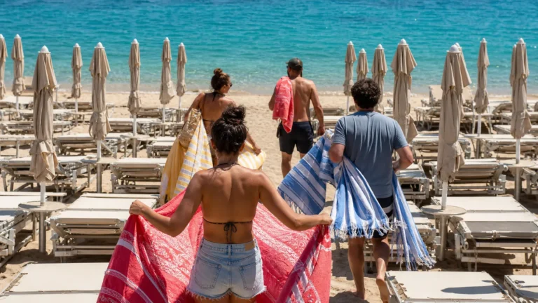 Plażowicze z własnymi ręcznikami przechodzą między rzędami pustych płatnych leżaków