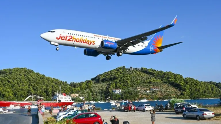 Samolot Jet2holidays podchodzi nisko do lądowania na Skiathos nad parkingiem z turystami i skuterami